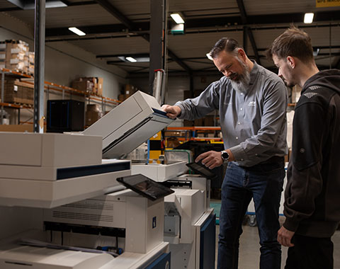 Two people in a warehouse operate and inspect a large printer for industrial use together
