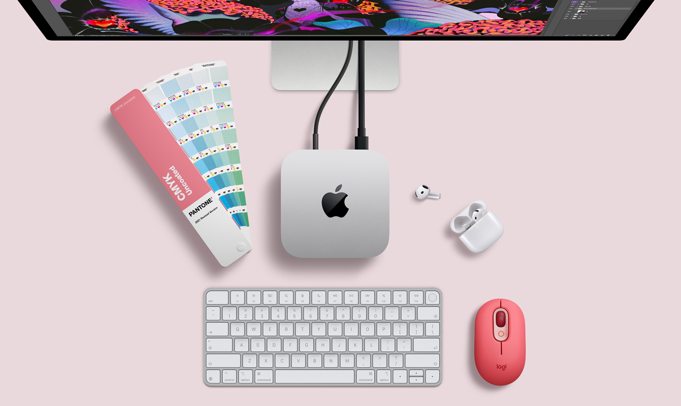 Creative workspace featuring an Apple Mac mini M6, Studio Display, keyboard, AirPods, color swatches, and a red mouse on a pink desk.