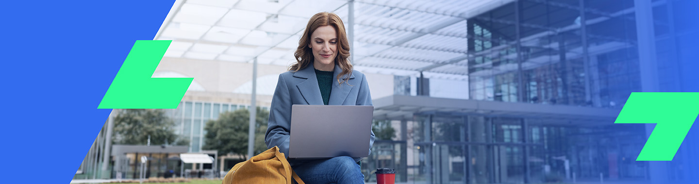 Woman sitting outdoors in front of modern building working focused on laptop at digital workspace