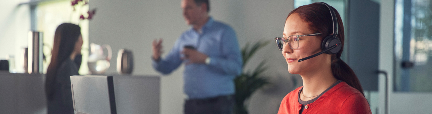 Woman wearing Epos headset working focused in modern office, colleague talking in the background