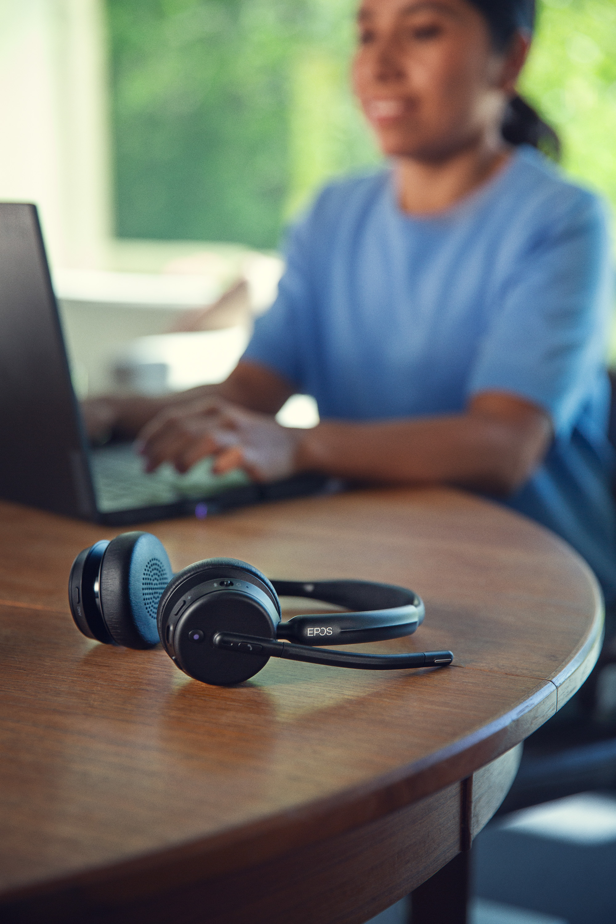 Wireless Epos headset on wooden table in front of person working on laptop and talking