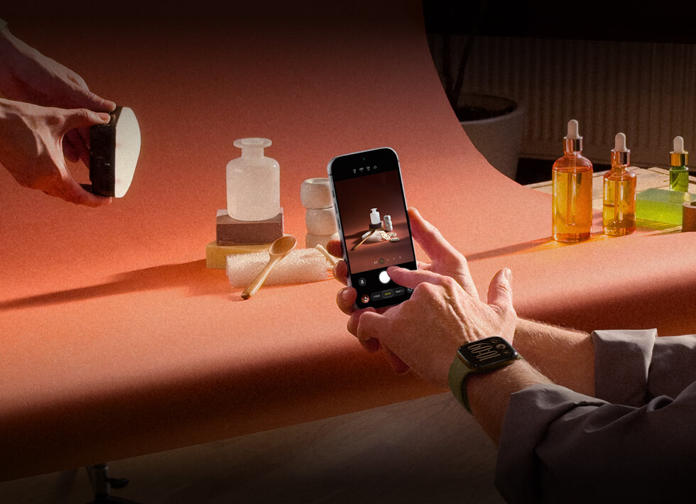 Person photographing a product setup of cosmetic items with studio lighting and props using a smartphone